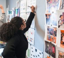 Student writing notes on paper pinned to a cork board. Click to learn more about the Curricula Committee.